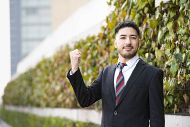 Karışık ırktan, takım elbiseli, sakallı genç bir işadamı. Yumruk tutuyor ve destekliyor.