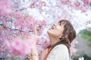Asyalı genç bir kadın baharda çiçek açan kiraz çiçeklerinin tadını çıkarıyor.