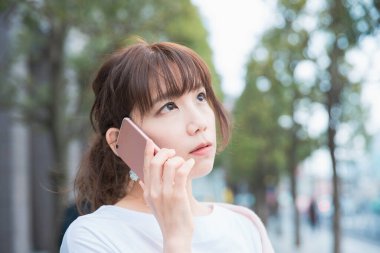 Genç Asyalı kadın dışarıda akıllı telefon kullanarak sohbet ediyor.