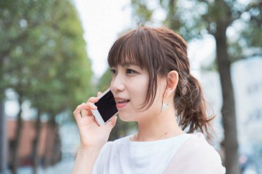 Genç Asyalı kadın dışarıda akıllı telefon kullanarak sohbet ediyor.
