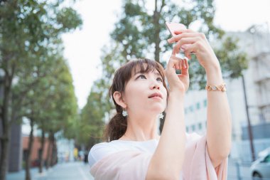 Akıllı telefon kullanan, fotoğraf çeken ve uygulamalar kullanan Asyalı bir kadın.