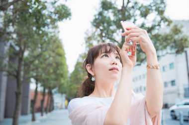 Akıllı telefon kullanan, fotoğraf çeken ve uygulamalar kullanan Asyalı bir kadın.