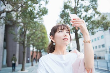 Akıllı telefon kullanan, fotoğraf çeken ve uygulamalar kullanan Asyalı bir kadın.