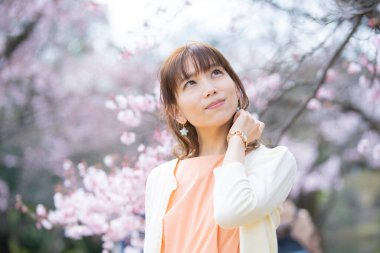 Asyalı genç bir kadın baharda çiçek açan kiraz çiçeklerinin tadını çıkarıyor.