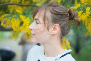 Beyaz tenli genç bir kadın çiçek açan mimoza çiçeklerine bakıyor.