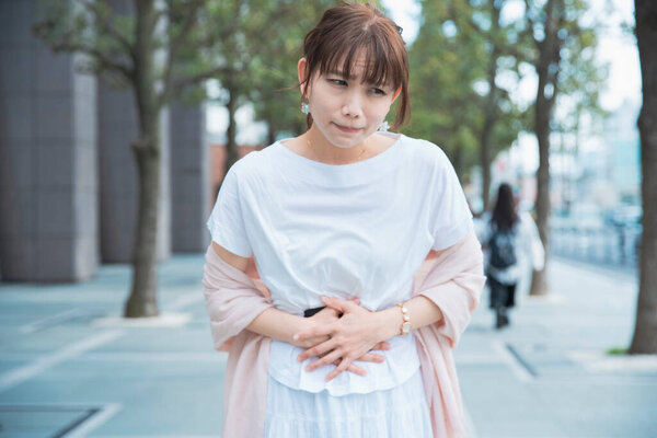 Молодая азиатка держится за руки с болью в животе на открытом воздухе
