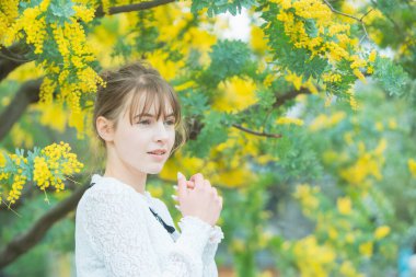 Beyaz tenli genç bir kadın çiçek açan mimoza çiçeklerine bakıyor.