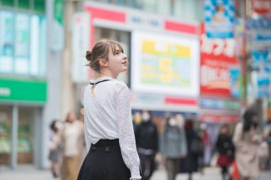 Genç Avrupalı kadın gülümseyerek Shibuya şehir merkezini (Tokyo, Japonya) geziyor.