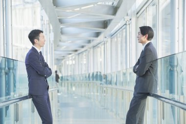 İki Asyalı iş adamı sosyal bir mesafede sohbet ediyorlar.