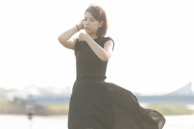 Deniz kenarındaki bir parkta siyah elbiseli Asyalı genç bir kadın.