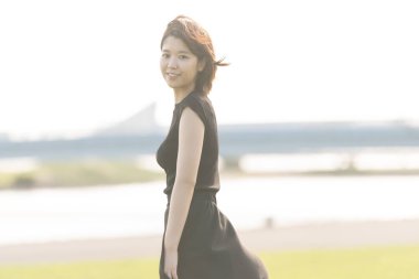 Deniz kenarındaki bir parkta siyah elbiseli Asyalı genç bir kadın.