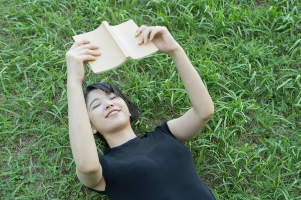 Parkta çimenli bir kitap okuyan Asyalı üniversite öğrencisi.