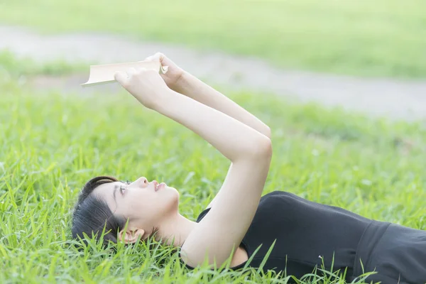 Parkta çimenli bir kitap okuyan Asyalı üniversite öğrencisi.
