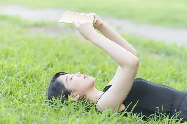 Parkta çimenli bir kitap okuyan Asyalı üniversite öğrencisi.