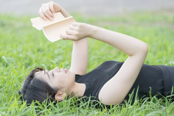 Parkta çimenli bir kitap okuyan Asyalı üniversite öğrencisi.