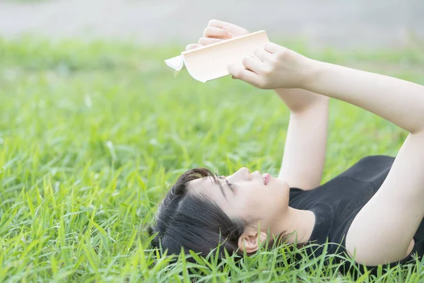 Parkta çimenli bir kitap okuyan Asyalı üniversite öğrencisi.