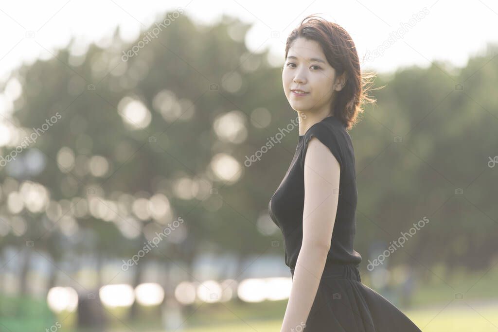 Asian (Japanese) young woman in a black dress in a park by the sea