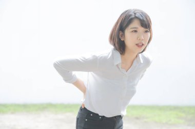 Sırtı ağrıyan Asyalı genç bir kadın elleri kalçasında