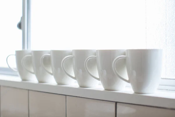 Białe Filiżanki Kawy Ustawione Rzędzie Przy Oknie Pokoju Mieszkalnym — Zdjęcie stockowe
