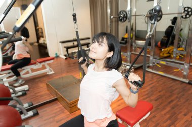 Asyalı kadın kişisel spor salonunda aletlerle kas eğitimi alıyor.