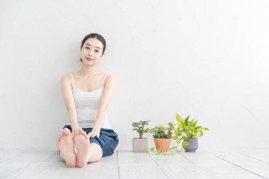 Asyalı genç kadın aydınlık bir odada hafif bir egzersiz yapıyor.