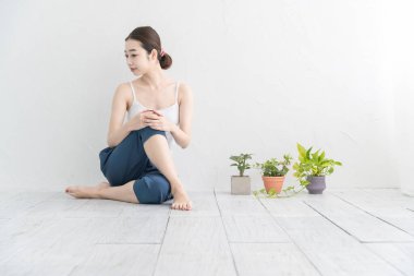 Asyalı genç kadın aydınlık bir odada hafif bir egzersiz yapıyor.