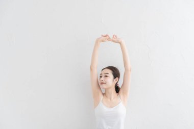 Asyalı genç kadın aydınlık bir odada hafif bir egzersiz yapıyor.