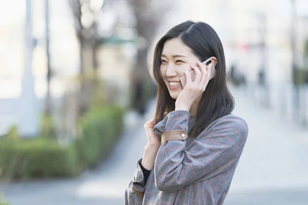 Asyalı Genç Bir Kadın Kulağında Akıllı Telefon Olan Biriyle Konuşuyor — Stok fotoğraf