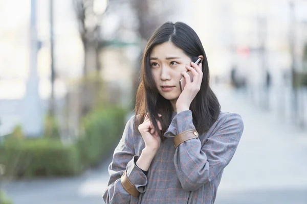 アジアの若い女性は耳にスマートフォンを持つ誰かと話して — ストック写真