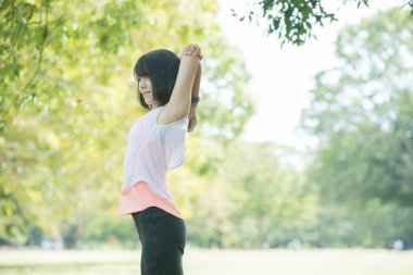 Yeşillik dolu bir parkta gerinen Asyalı genç bir kadın.
