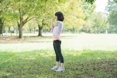 Yeşillik dolu bir parkta gerinen Asyalı genç bir kadın.