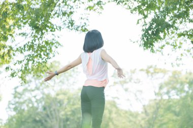Parkta egzersiz yaparken derin bir nefes alan Asyalı kadın.