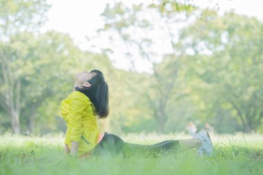 Yeşillik dolu bir parkta gerinen Asyalı genç bir kadın.