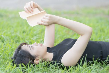 Parkta çimenli bir kitap okuyan Asyalı üniversite öğrencisi.