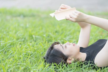 Parkta çimenli bir kitap okuyan Asyalı üniversite öğrencisi.