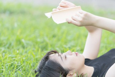 Parkta çimenli bir kitap okuyan Asyalı üniversite öğrencisi.