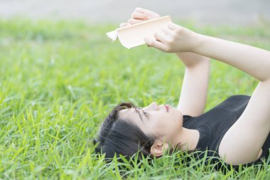 Parkta çimenli bir kitap okuyan Asyalı üniversite öğrencisi.