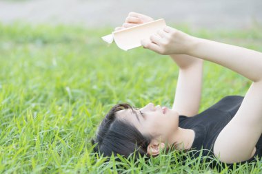 Parkta çimenli bir kitap okuyan Asyalı üniversite öğrencisi.