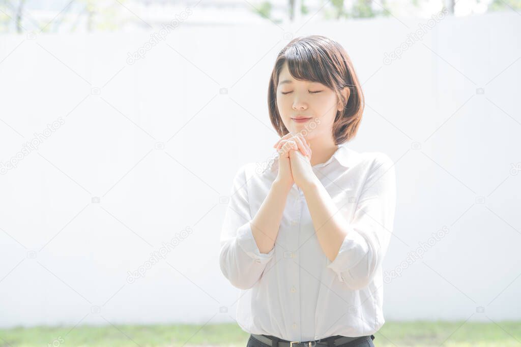 Young Asian woman posing in prayer with hands together outdoors