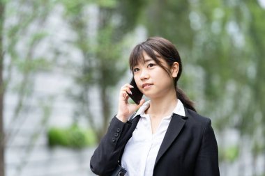 Asyalı genç bir kadın kulağında akıllı telefon olan biriyle konuşuyor.
