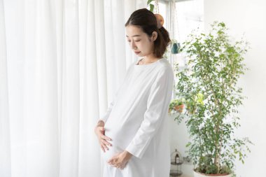 Asyalı hamile kadın huzursuz bir ifadeyle karnına dokunuyor.