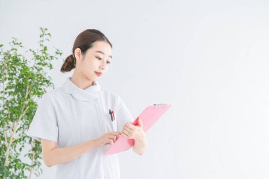 Bir Asyalı (Japon) kadın hemşirenin portresi. Kapalı alanda tıbbi kayıtlara bakıyor.