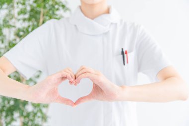 Bir Asyalı (Japon) kadın hemşirenin portresi elle kalp şekli oluşturuyor.