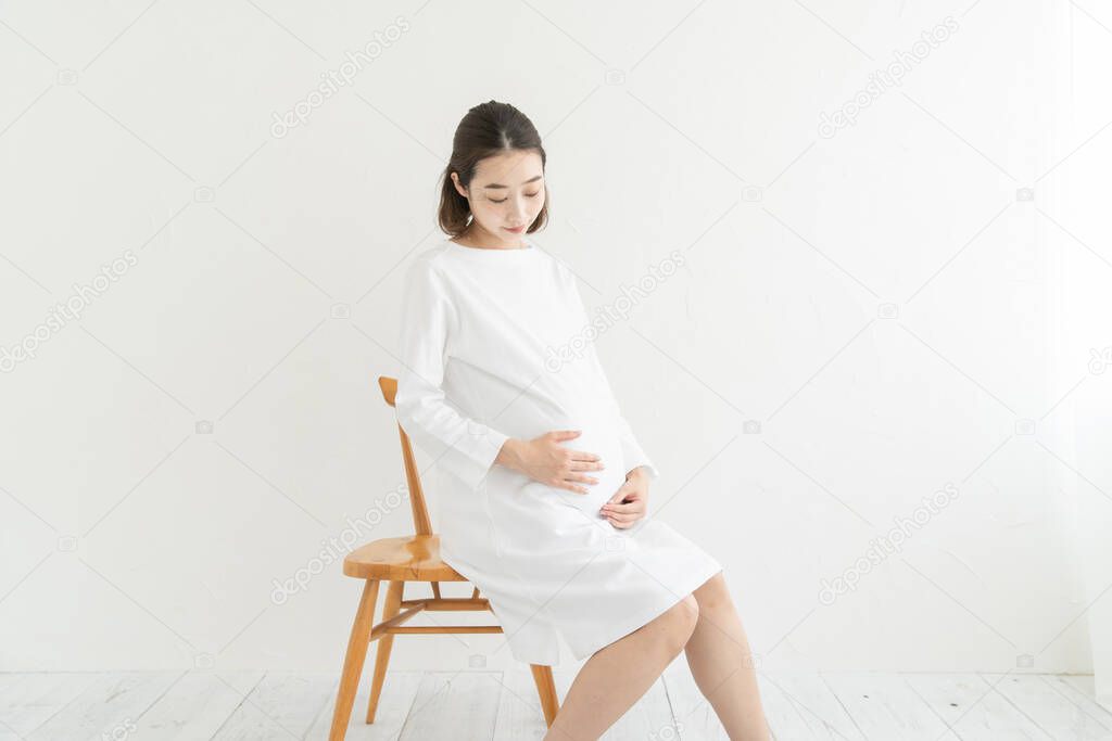 Asian (Japanese) young pregnant woman in a white dress touching her abdomen