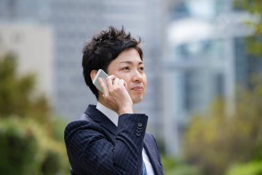 Bir iş bölgesinin caddesinde akıllı telefon kullanarak iletişim kuran Asyalı bir işadamı