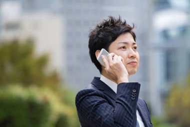 Bir iş bölgesinin caddesinde akıllı telefon kullanarak iletişim kuran Asyalı bir işadamı