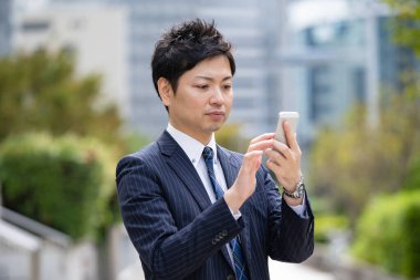 Bir iş bölgesinin caddesinde akıllı telefon kullanarak iletişim kuran Asyalı bir işadamı