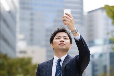 Bir iş bölgesinin caddesinde akıllı telefon kullanarak iletişim kuran Asyalı bir işadamı