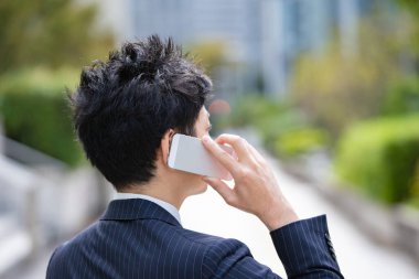 Bir iş bölgesinin caddesinde akıllı telefon kullanarak iletişim kuran Asyalı bir işadamı