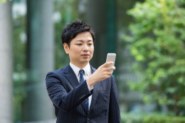 Bir iş bölgesinin caddesinde akıllı telefon kullanarak iletişim kuran Asyalı bir işadamı